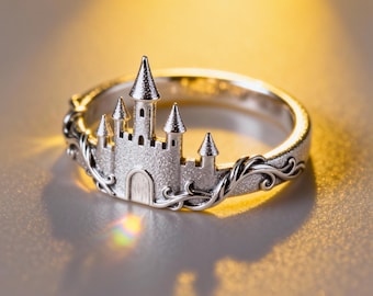 May include: A silver-toned ring featuring a central castle motif with four pointed turrets and a textured finish. The band is adorned with intricate, raised scrollwork patterns that extend from the base of the castle along the sides of the ring.