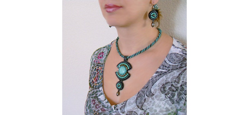 May include: A turquoise and black beaded necklace with a large turquoise pendant. The necklace is worn by a person with a white and black patterned blouse.