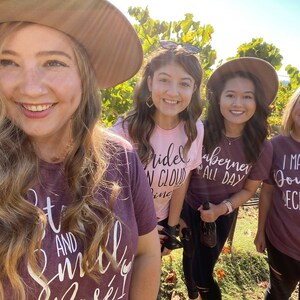 May include: Four friends wearing maroon and pink t-shirts with wine-themed text. The text on the shirts reads "Bride in Cloud Nine", "Cabernet All Day", "I Make My Own Decisions", and "Sit and Smell the Wine".