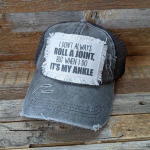 May include: A black and grey trucker hat with a white patch that reads "I don't always roll a joint, but when I do it's my ankle".