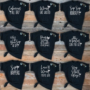 May include: Nine black t-shirts with white text and wine glass graphics. The shirts feature sayings like "Cabernet All Day", "Wine Girl Wasted", "Sip Sip Hooray!" and "Love the Wine You're With".