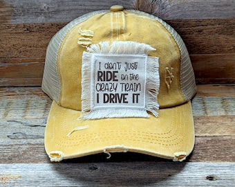 May include: A yellow distressed trucker hat with a white patch that reads "I don't just ride on the crazy train I drive it".
