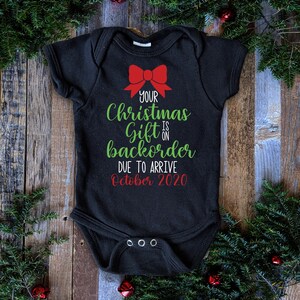 Könnte beinhalten: Schwarzer Baby-Strampler mit einer roten Schleife und grünem Text, der lautet: "Dein Weihnachtsgeschenk ist auf Vorbestellung und wird voraussichtlich im Oktober 2020 eintreffen."