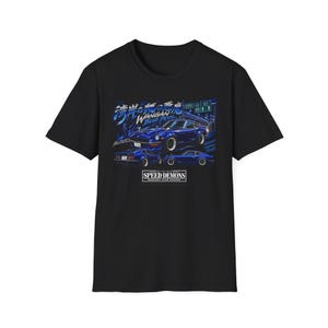 Puede incluir: Una camiseta negra de manga corta con un estampado gráfico de un coche deportivo azul. El diseño incluye texto en japonés, las palabras WANGAN BLUE DEVIL y un recuadro en la parte inferior con el texto SPEED DEMONS MIDNIGHT CLUB RACERS.