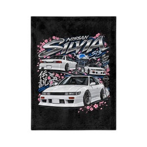May include: A black fleece blanket featuring a graphic print of three white Nissan Silvia S13 cars. The design includes pink cherry blossoms, a Japanese torii gate, Mount Fuji, and the text Nissan Silvia S13, No Limits Just Drive, and Street Legend.