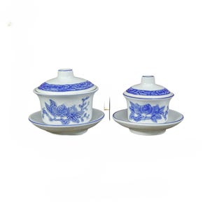May include: Two white porcelain tea sets with blue floral designs. Each set includes a lidded cup and a saucer. The cups and lids have blue trim. The floral design is a detailed blue pattern.