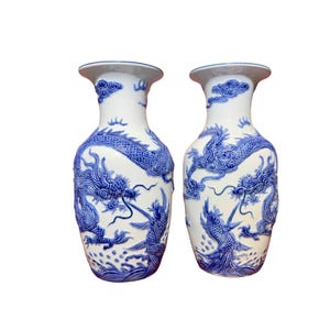 May include: Two white ceramic vases with blue dragon and cloud designs. The vases have a flared rim and a bulbous body. The dragon design is intricately detailed, and the vases are likely decorative items.