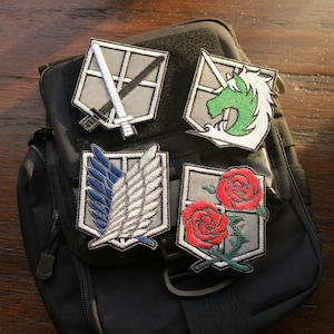 May include: Four embroidered patches with different designs are displayed on a black bag. The patches feature a sword, a unicorn, wings, and red roses. Each patch has a gray background and a white border.