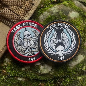 May include: Two round embroidered patches with the text "TASK FORCE" and the number "141". One patch has a red border and a skull with wings. The other patch has a black border and a skull with wings.