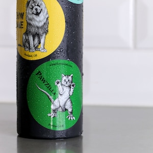 Pode incluir: Um adesivo verde e branco com uma ilustra&ccedil;&atilde;o em preto e branco de um gato com garras. O adesivo diz "PAWZILLA" e "Portland, OR".