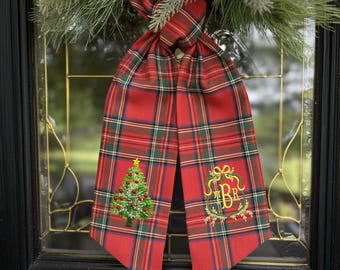 May include: A red plaid Christmas door decoration with a green Christmas tree and gold star embroidery. The decoration also features a gold monogram and is hanging on a glass door.