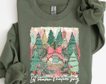 May include: An olive green sweatshirt with a festive Christmas design. The graphic includes a pink bow, Christmas trees, and the text "Let heaven & nature sing". The sweatshirt is made of a soft material.