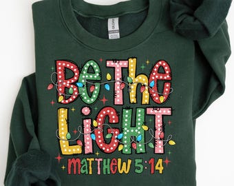 宗教的なクリスマススウェットシャツ：Be The Light、インスピレーションあふれるクリスチャンTシャツ、ファミリークリスマススウェットシャツ、クリスマスライトTシャツ