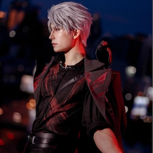May include: A person with gray hair and red eyes, wearing a black shirt with red accents and a dark gray jacket. The outfit includes a black belt and a strap across the chest. The background is blurred with city lights.