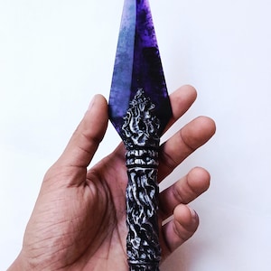 May include: A decorative kunai knife with a purple blade and a detailed, ornate handle. The handle is silver and black with a ring at the base. The blade is a deep purple color.