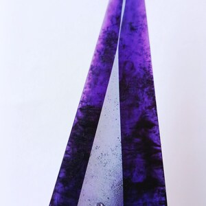 May include: A tall, abstract sculpture with a pointed top. The sculpture features a deep purple, marbled design with black accents. A silver-colored, textured base is visible at the bottom, adding contrast to the design.