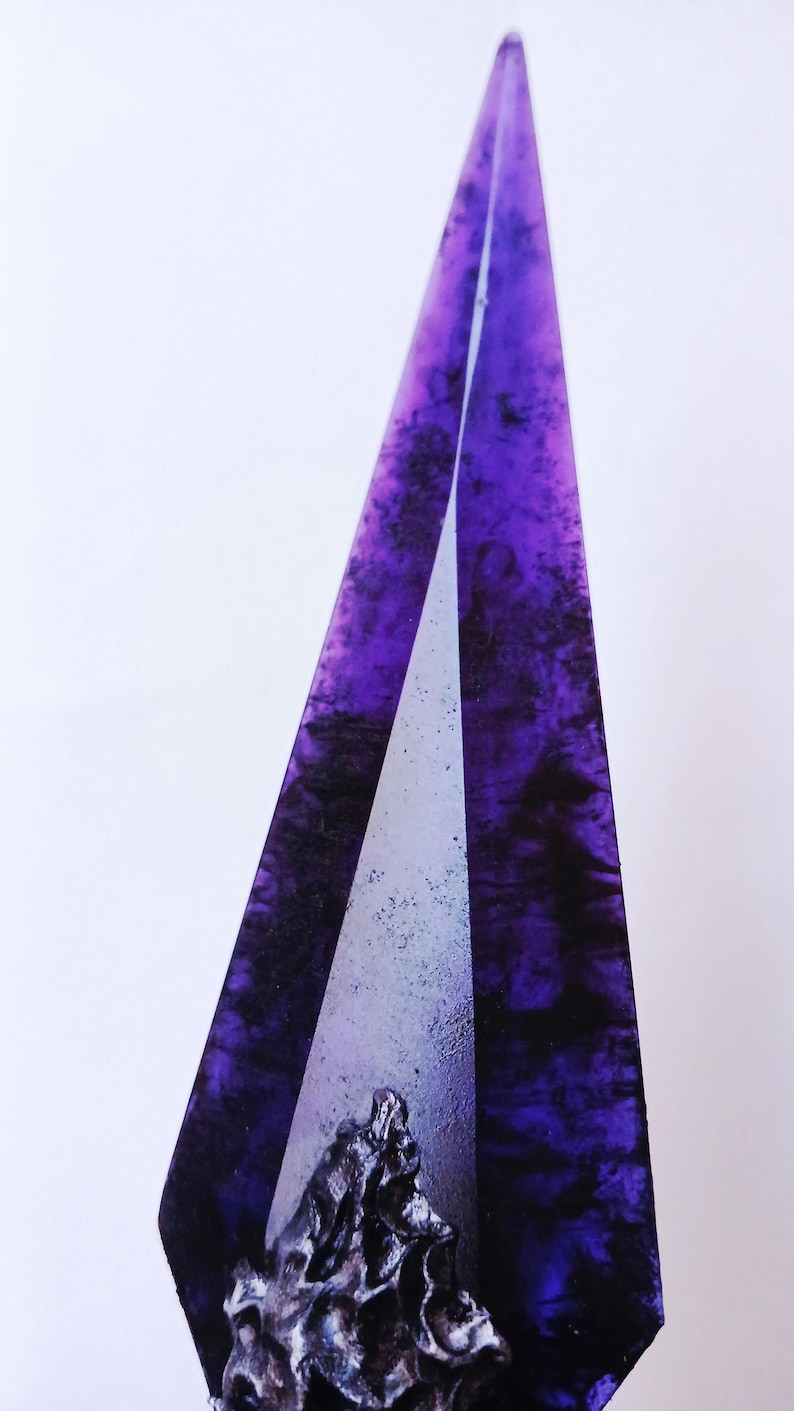 May include: A tall, abstract sculpture with a pointed top. The sculpture features a deep purple, marbled design with black accents. A silver-colored, textured base is visible at the bottom, adding contrast to the design.