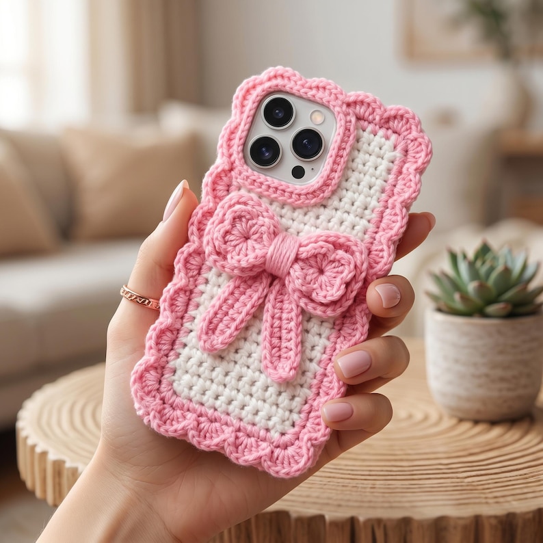 Puede incluir: Funda de tel&eacute;fono de ganchillo blanca y rosa con dise&ntilde;o de lazo. La funda tiene un borde festoneado y un lazo rosa en el centro. La funda est&aacute; dise&ntilde;ada para un tel&eacute;fono inteligente.