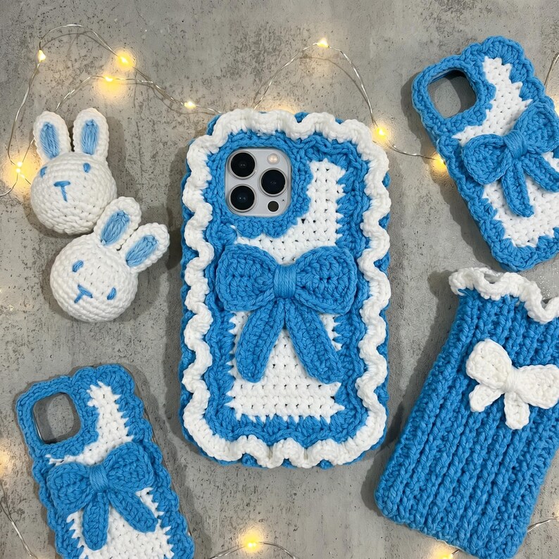 Puede incluir: Una colecci&oacute;n de fundas de tel&eacute;fono y accesorios con forma de conejito hechos a mano con ganchillo. Las fundas son blancas con ribetes y lazos azules. Tambi&eacute;n hay dos peque&ntilde;os conejitos blancos con detalles azules.