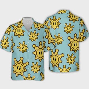 Puede incluir: Camisa azul claro con botones y un patrón repetido de personajes amarillos con forma de placa de sheriff. La camisa de manga corta tiene cuello y botones en la parte delantera. El diseño es de estilo juguetón y de dibujos animados.