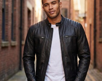 May include: A black leather jacket with a quilted shoulder design and a stand-up collar. The jacket has two zippered pockets on the chest and a front zipper closure. The person is wearing a white t-shirt underneath the jacket.