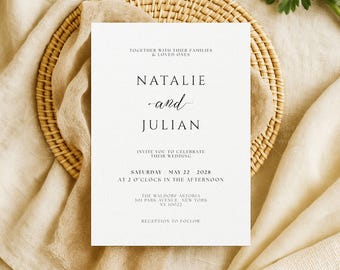 May include: A wedding invitation with the names "Natalie and Julian" in elegant script. The invitation is on a white card, with the date and time of the wedding printed below. The card is placed on a woven placemat and beige fabric.