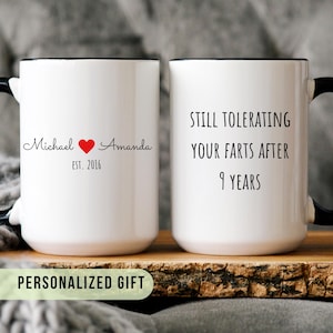Puede incluir: Taza de cerámica blanca con asa y borde negros. Un lado dice "Michael ❤️ Amanda EST. 2016." El otro lado dice "Still tolerating your farts after 9 years."
