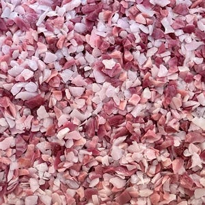 May include: Close-up of a pile of crushed, irregularly shaped stones. The stones are a mix of light pink and deep rose colors, creating a textured, mosaic-like appearance. The pieces vary in size and shape.