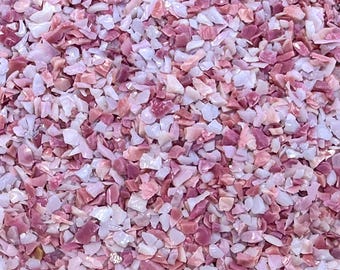May include: A collection of small, irregularly shaped crushed stone fragments in varying shades of pink, light rose, and translucent white. The pieces are densely packed together, creating a textured surface with a mix of matte and glossy finishes.