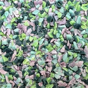 Könnte beinhalten: Nahaufnahme eines Haufens farbiger, unregelmäßig geformter Glasstücke. Die Stücke sind in Grüntönen, Blaugrün und blassem Rosa gehalten. Das Glas scheint recycelt zu sein, mit einer strukturierten, matten Oberfläche. Die Stücke variieren in Größe und Form.
