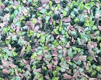 May include: A close-up view of a pile of colorful, irregularly shaped glass pieces. The pieces are in shades of green, blue-green, and pale pink. The glass appears to be recycled or repurposed, with a textured, matte finish. The pieces vary in size and shape.