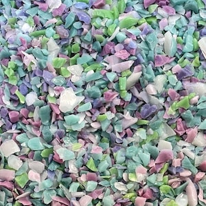 May include: Close-up of a pile of colorful, irregularly shaped pieces. The pieces are in shades of light blue, green, purple, pink, and white. The texture appears to be smooth and possibly translucent, suggesting a material like glass or plastic.