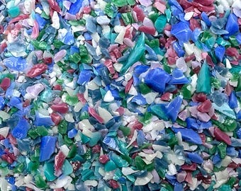 May include: A close-up view of a colorful assortment of crushed glass pieces. The fragments are in various shapes and sizes, with a mix of colors including blue, green, red, white, and pink. The pieces are scattered, creating a textured and vibrant appearance.