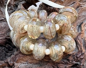 May include: A collection of 18 glass beads with a swirling, marbled pattern in shades of brown, beige, and gold. The beads have a glossy finish and are strung together with white beads.