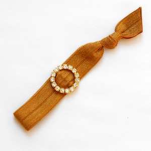 May include: A mustard yellow elastic hair tie with a gold-toned ring adorned with clear rhinestones.