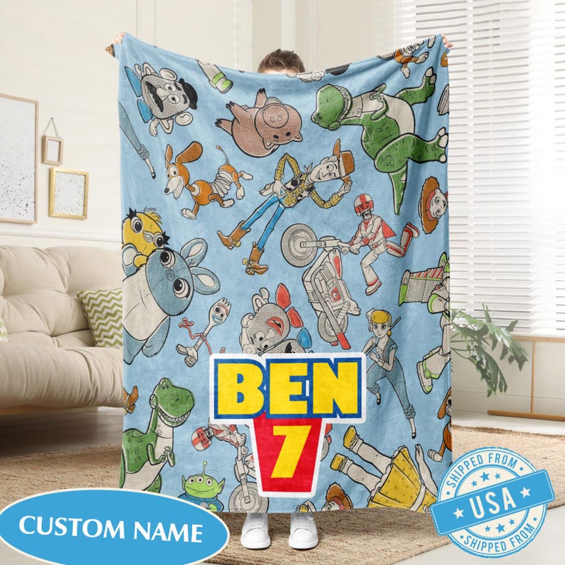 May include: A light blue blanket featuring cartoon characters from the Toy Story franchise. The blanket has a repeating pattern of characters like Woody, Buzz Lightyear, and Rex. The blanket has the text "BEN 7" in a yellow and red design, and a blue banner that says "CUSTOM NAME".