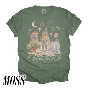 Pode incluir: Camiseta verde musgo com uma ilustra&ccedil;&atilde;o detalhada dos marcos da Walt Disney World, incluindo o Castelo da Cinderela e a Spaceship Earth. O texto diz "Walt Disney World Est. 1971" e "The Most Magical Place On Earth."