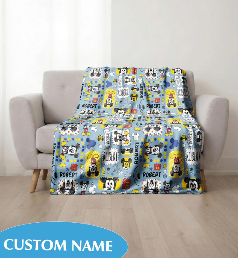 Puede incluir: Una manta azul claro con un patr&oacute;n repetido de Mickey Mouse, estrellas y el nombre "ROBERT". La manta est&aacute; sobre un sof&aacute; gris. Las palabras "CUSTOM NAME" est&aacute;n en la parte inferior.