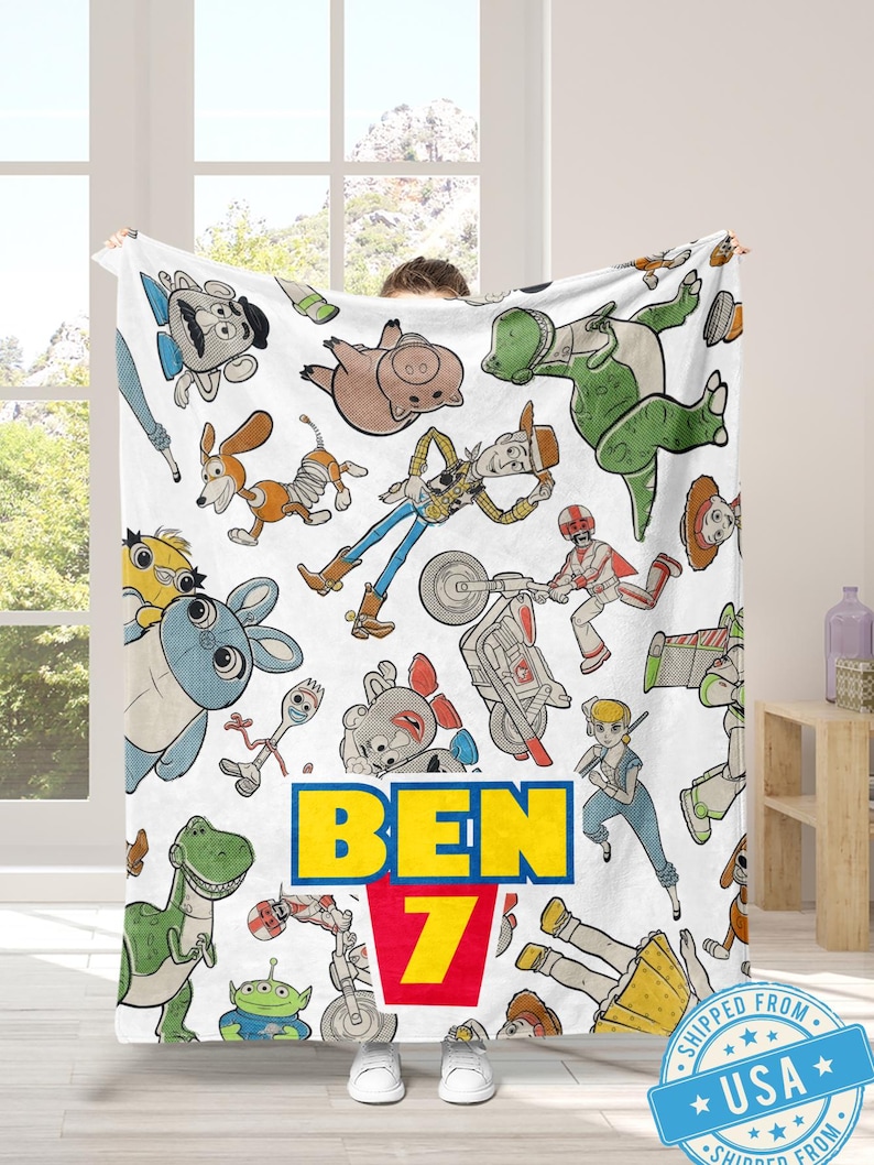 May include: White blanket featuring colorful cartoon characters from the Toy Story franchise. The blanket has a repeating pattern of characters and the name "BEN 7" in yellow and red. The blanket is made of a soft material.