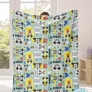 Puede incluir: Una manta azul claro con un patr&oacute;n repetido de ilustraciones de Mickey Mouse y el nombre "ROBERT" en un marco rectangular. El dise&ntilde;o incluye acentos amarillos, rojos y azules, creando una est&eacute;tica l&uacute;dica y colorida.