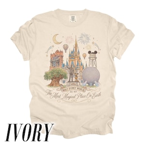 Pode incluir: Camiseta marfim com uma ilustra&ccedil;&atilde;o detalhada dos marcos da Walt Disney World, incluindo o Castelo da Cinderela, Spaceship Earth e o Hollywood Tower Hotel. A camisa inclui o texto "Walt Disney World Est. 1971" e "The Most Magical Place On Earth."
