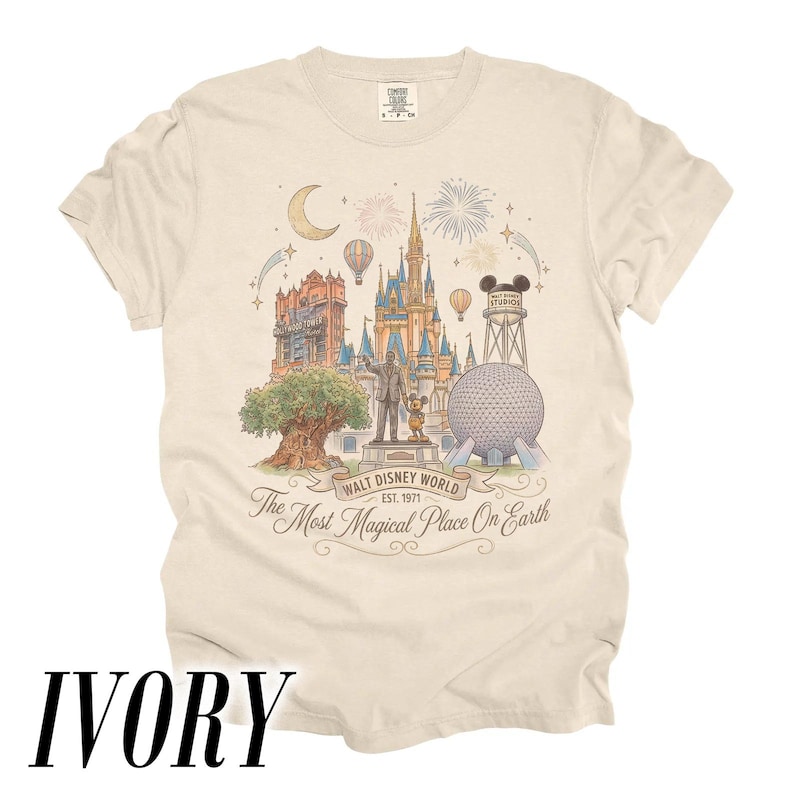 Pode incluir: Camiseta marfim com uma ilustra&ccedil;&atilde;o detalhada dos marcos da Walt Disney World, incluindo o Castelo da Cinderela, Spaceship Earth e o Hollywood Tower Hotel. A camisa inclui o texto "Walt Disney World Est. 1971" e "The Most Magical Place On Earth."