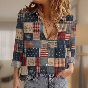 May include: A long-sleeve button-down shirt featuring a patchwork design of red, white, and blue patterns. The fabric displays stars, stripes, and plaid squares, with printed text reading USA 250 and 1776-2026 within circular laurel wreath motifs.