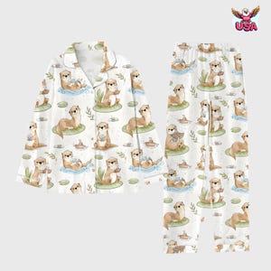 Puede incluir: Conjunto de pijama blanco con un estampado repetido de nutrias de dibujos animados sobre nen&uacute;fares, barcos y hojas. La parte superior de manga larga tiene una tapeta con botones y un cuello con muescas. Los pantalones a juego tienen cintura el&aacute;stica. Las nutrias est&aacute;n en varias poses.