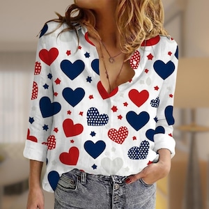 May include: White button-down shirt with a pattern of red, white, and blue hearts and stars. The long-sleeved shirt has a V-neck collar and is made of a lightweight fabric. The shirt is a festive and patriotic design.