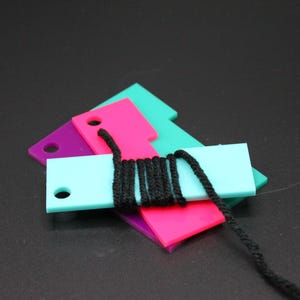 May include: A close-up of a black string wrapped around three plastic pieces. The pieces are layered on top of each other and are turquoise, pink, and purple.