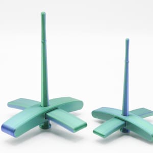 May include: Two abstract sculptures with a cross-shaped base and a vertical rod. The sculptures have a gradient color scheme, transitioning from green to blue. The bases are cross-shaped with rounded edges, and the rods are cylindrical.
