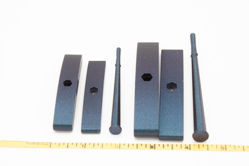 May include: A set of six dark blue metallic tools including four rectangular blocks with central hexagonal holes and two tapered cylindrical rods, arranged horizontally above a yellow measuring tape showing five inches in total length.