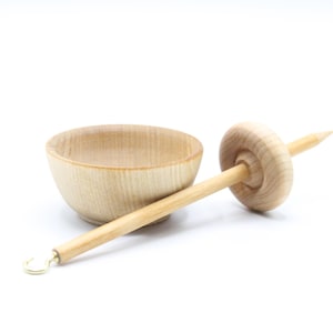 May include: A wooden spinning wheel with a bowl for holding fiber. The wheel is made of light wood and has a simple design.