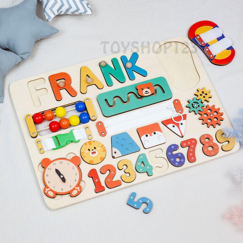 K&ouml;nnte beinhalten: Holz-Lernspielzeug mit dem Namen "FRANK" in bunten Buchstaben. Enth&auml;lt eine Uhr, einen Abakus, Zahlen, Formen und Puzzles mit Tiermotiven. Enth&auml;lt ein rotes, gelbes und blaues Spielzeug oben rechts.